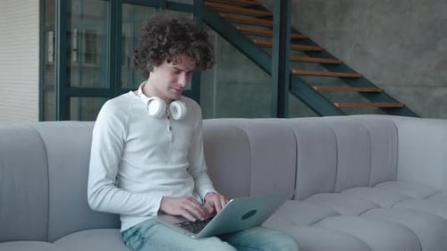 Young Guy in Leaning on Comfortable Sofa Working Remotely on Computer From Home