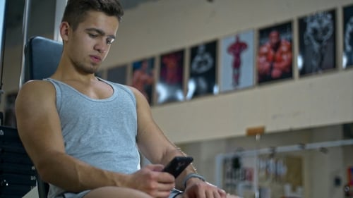 Athletic Man Sitting in Fitness Gym After Workout, Chatting Online Smart Phone