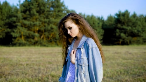 Young Brunette in Denim Posing Sensually on Background of Trees in Field