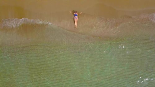Frau im Bikini liegt am Sandstrand und Wellen waschen ihre Füße