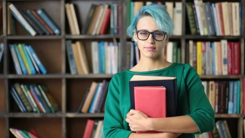 Woman Holding Books Smiling In Front of Bookshelf