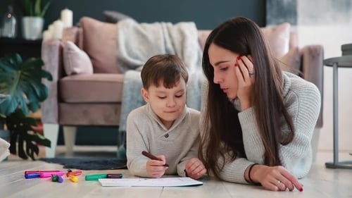 Woman and Boy Drawing Together on Floor Indoors