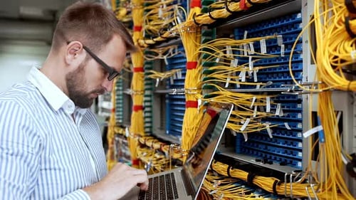 Server Technician Works With Laptop on Network Cables