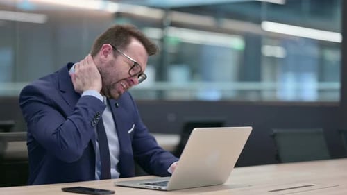 Man in Suit Typing on Laptop Rubbing Neck