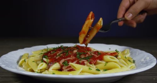 Fork takes pasta with tomato sauce from plate