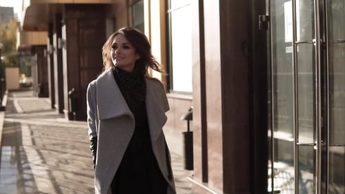 Charming Young Woman Walks Through the Autumn City in a Coat and Smiles