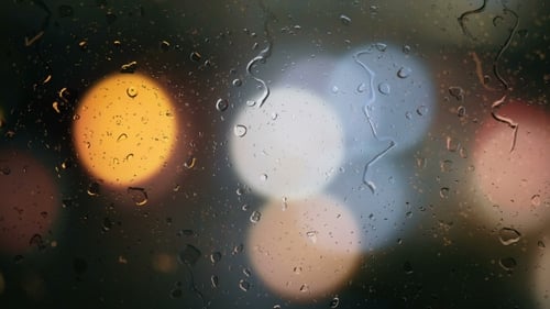 Regentropfen auf einem Autofenster mit verschwommenem Hintergrund von Straßenampeln