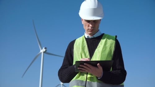 Engineer Using Digital Tablet Against Wind Turbine