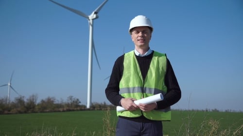 Smiling Engineer Standing Against Wind Farm