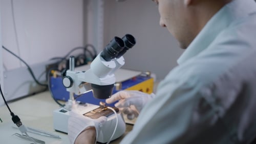 Engenheiro Eletrônico está examinando o telefone celular sob um microscópio, reparando o mecanismo