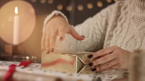 Woman Wrapping Christmas Gift with Red Ribbon