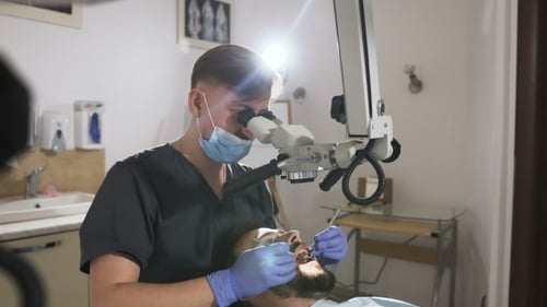 Doctor Dentist Using Dental Microscope in Modern Dental Office for Operation. Male Dentist