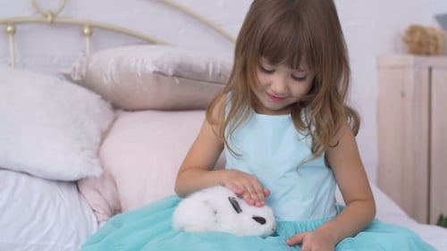 Girl Cuddles White Rabbit on Bed in Bedroom
