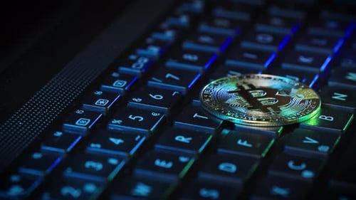 Pièce d'or Bitcoin posée sur un clavier RGB rétroéclairé, concept de technologie cryptographique