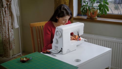 A Young Woman Is Working Behind an Electric Sewing Machine in the Atelier, a Lady Is Making a Stitch