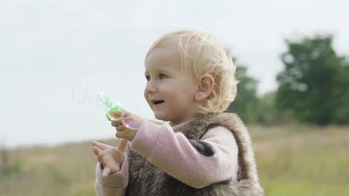 Cute Child Blowing Bubbles in a Grassy Field