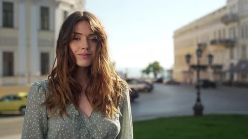 Porträt einer umgänglichen Sommerfrau im Kleid, die lächelt, während sie an einem sonnigen Tag in der Innenstadt spaziert, mit