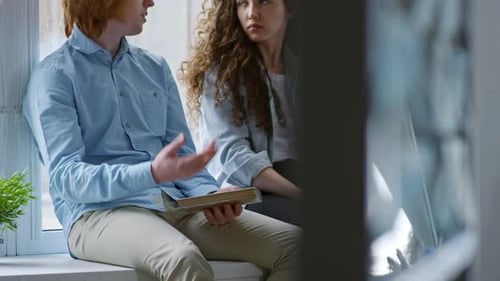 Jeunes collègues assis sur le rebord de la fenêtre au bureau et discutant du travail