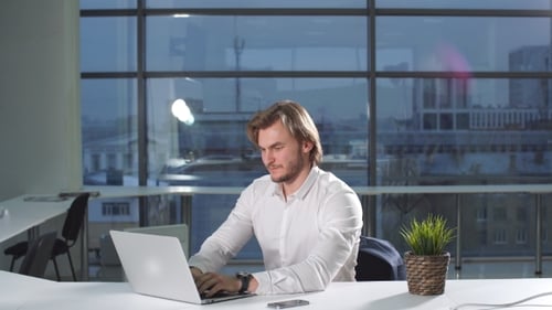 Porträt eines jungen attraktiven Geschäftsmannes, der am Schreibtisch arbeitet und Laptop im Büro benutzt.