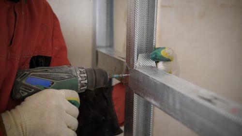 Construction Worker Drilling Metal Frame to Wall
