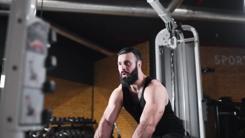 El hombre fuerte bombea los músculos en el gimnasio, los ejercicios de fuerza en los simuladores, el atleta en el gimnasio