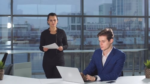 Man Works on Laptop, Woman Reviews Documents