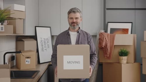Mature Man Holds Moving Box in Kitchen
