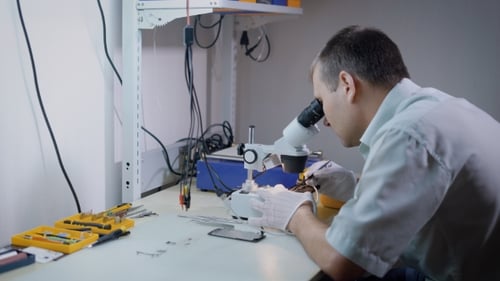 Man Using Microscope to Repair Small Device