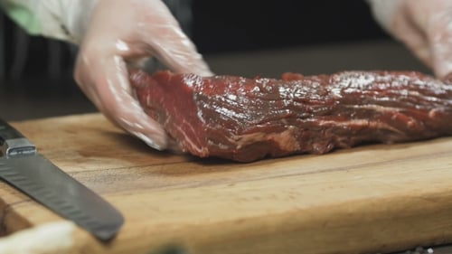 Chef cuts raw steak with knife on board