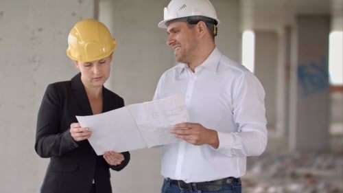 Two Architects Wearing Protective Helmet Works at Building Site