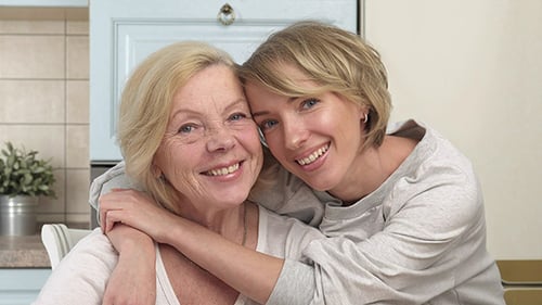 Woman Hugging Senior Woman Smiling in Kitchen