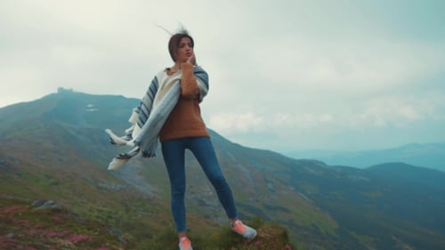 Attractive, Young, Fit Woman in a Sport Outfit and Stylish Poncho Standing on the Rocky Mountain Top