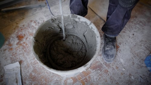 a Man Who Wears a Construction Suit Works with an Electric Drill, the Worker Breeds Cement