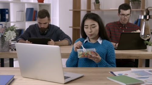 Asian Businesswoman Eating Salad at Desk in Office