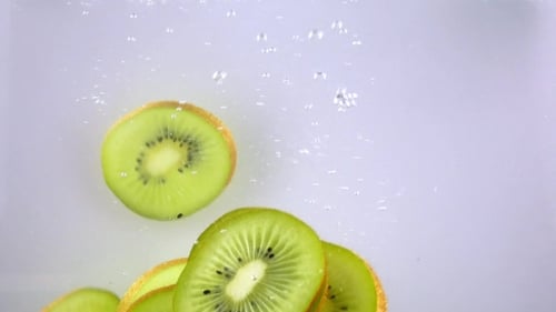 Kiwi Slices Dropping Into Water Creating Bubbles