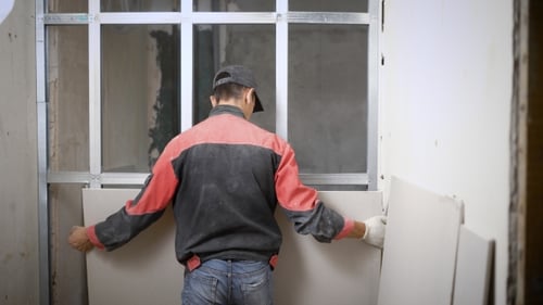 Man Covering Metal Construction of Wall with Panels on Building Site
