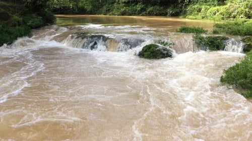 Standbild einer kleinen Kaskade, die das schnell fließende braune Wasser mit Wald im Hintergrund zeigt