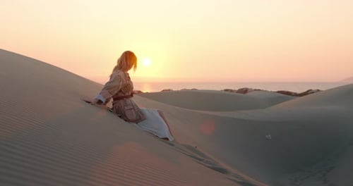 Blonde Woman Sits on Desert Dune at Sunset