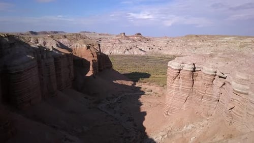 Flying over dry desert cliffs towards river bottoms filled with foliage