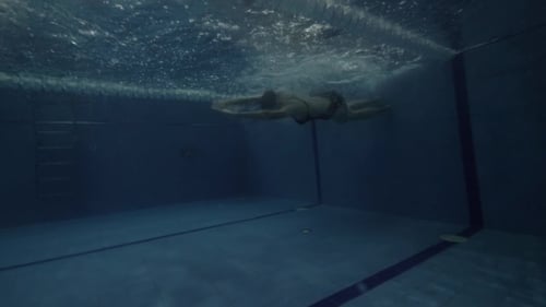 Sportliche Schwimmerin dreht sich unter Wasser und schwimmender Schmetterling im Pool