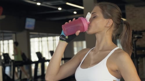 Thirsty Woman Drinking Cold Water From a Bottle After Endurance Training in Club
