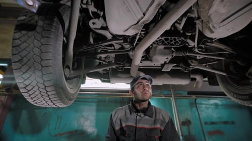 Professional Auto Mechanic Working on the Undercarriage of a Car in a Workshop.