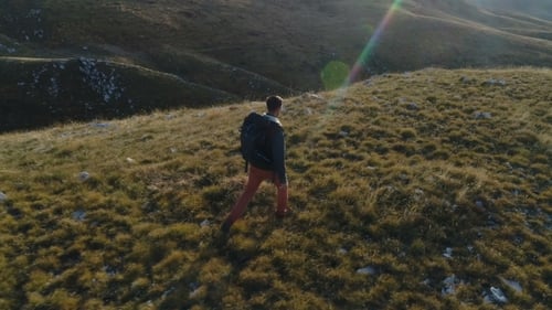 Man Hiking Through Rolling Grassy Hills with Backpack