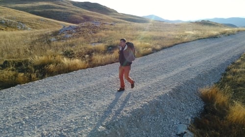Tourist with a Backpack Is Walking Along a Gravel Road