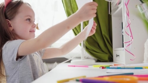 Glückliches kleines Mädchen führt einen Bleistift auf Papier und schaut sich das Zeichnen an