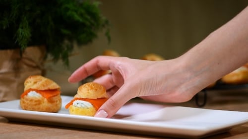 Weibliche Hände legen Profiteroles mit Lachs in einen weißen Teller