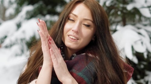 Chilled Young Woman with Long Dark Hair Is Standing in a Yard in Cold Winter Day, Warming Her Hands