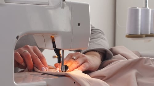 Woman Sews Pink Fabric on Sewing Machine, Close Up