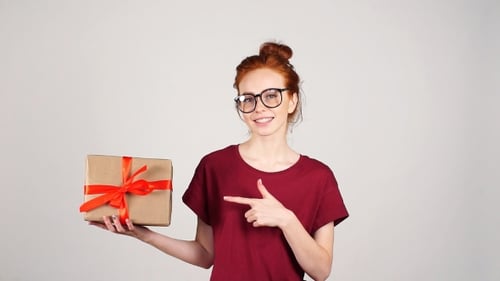 Smiling Woman Presents Gift with Red Ribbon