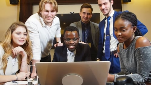 Smiling Business Team Gathers Around Laptop in Conference Room